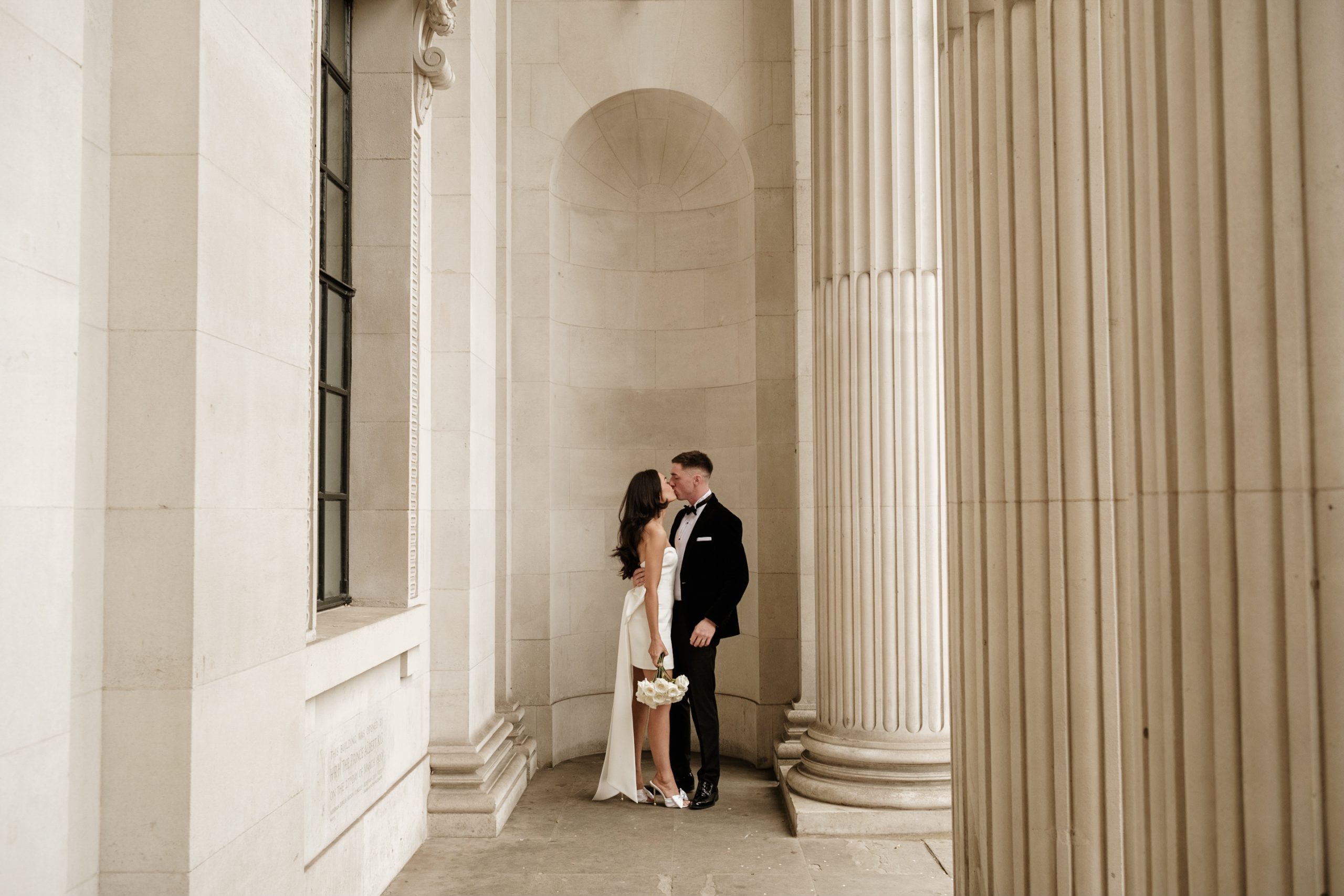 Bride and groom kissing in the arches of the iconic Old Marylebone town hall in central London