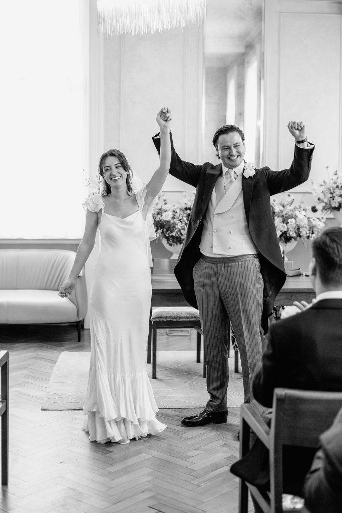 Bride and groom celebrating immediately after their wedding ceremony with guests applauding at Chelsea Old Town Hall in London.