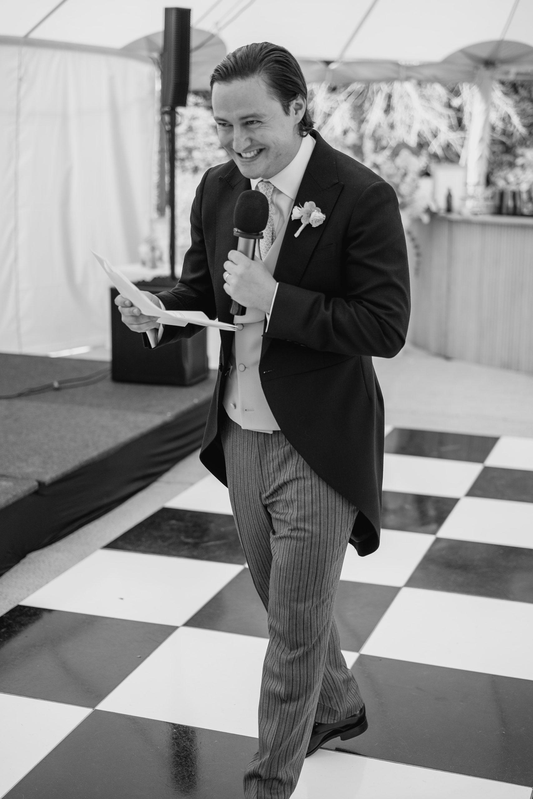 Groom giving an emotional speech on a black-and-white dance floor during a modern marquee wedding reception.