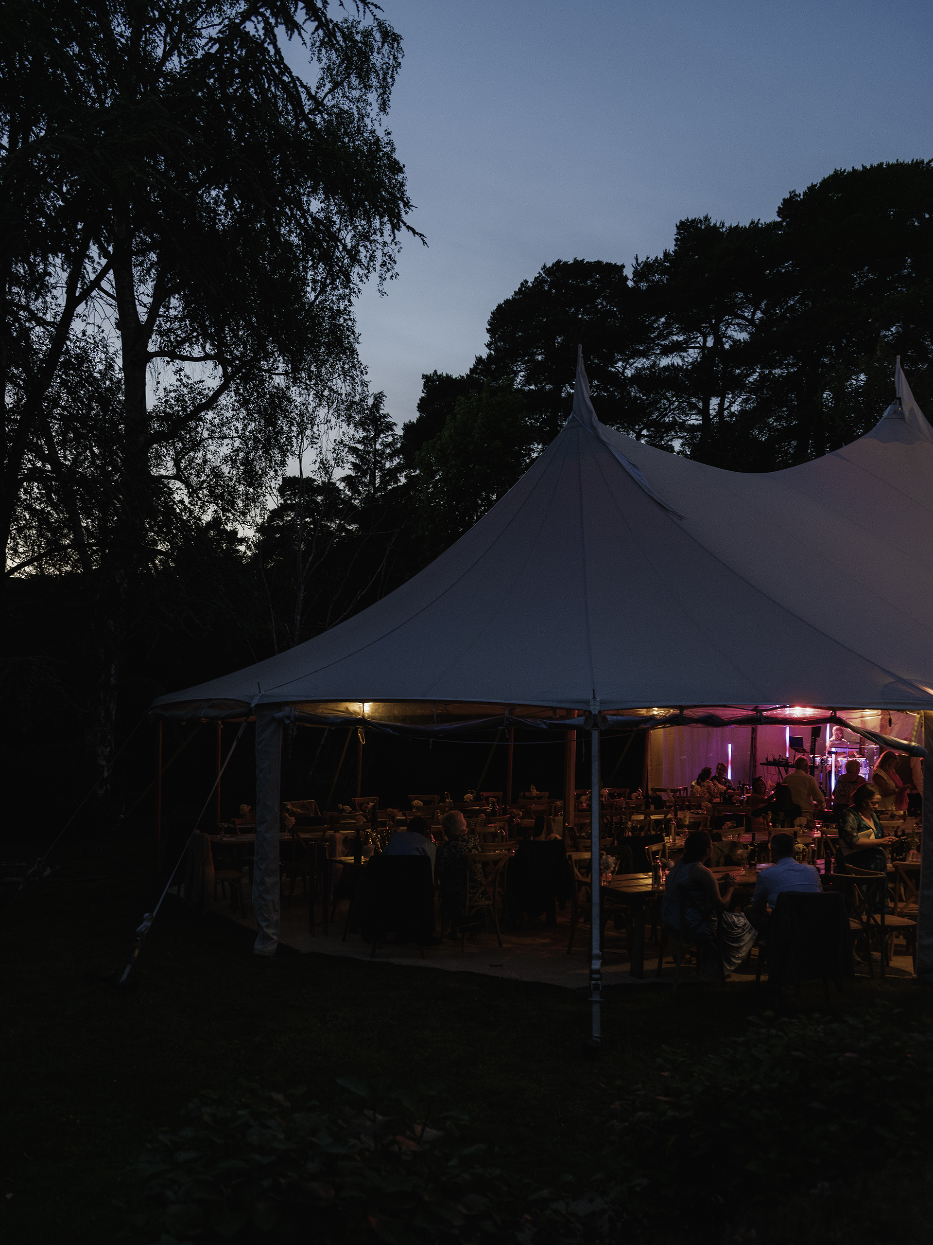 Evening wedding reception beneath a sailcloth marquee with ambient lighting at a modern outdoor wedding venue near London.