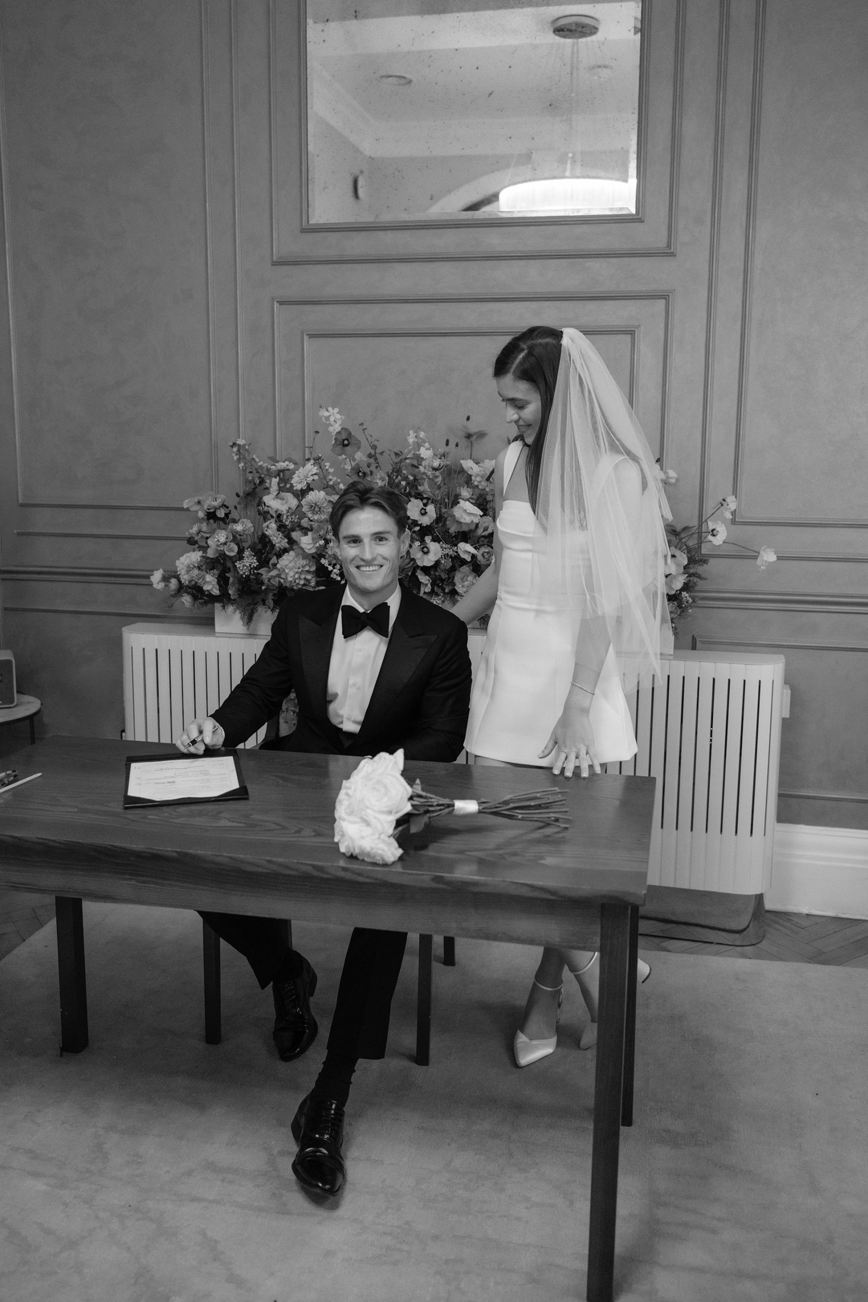 Groom signing the marriage register while the bride stands beside him during a modern London registry office wedding.