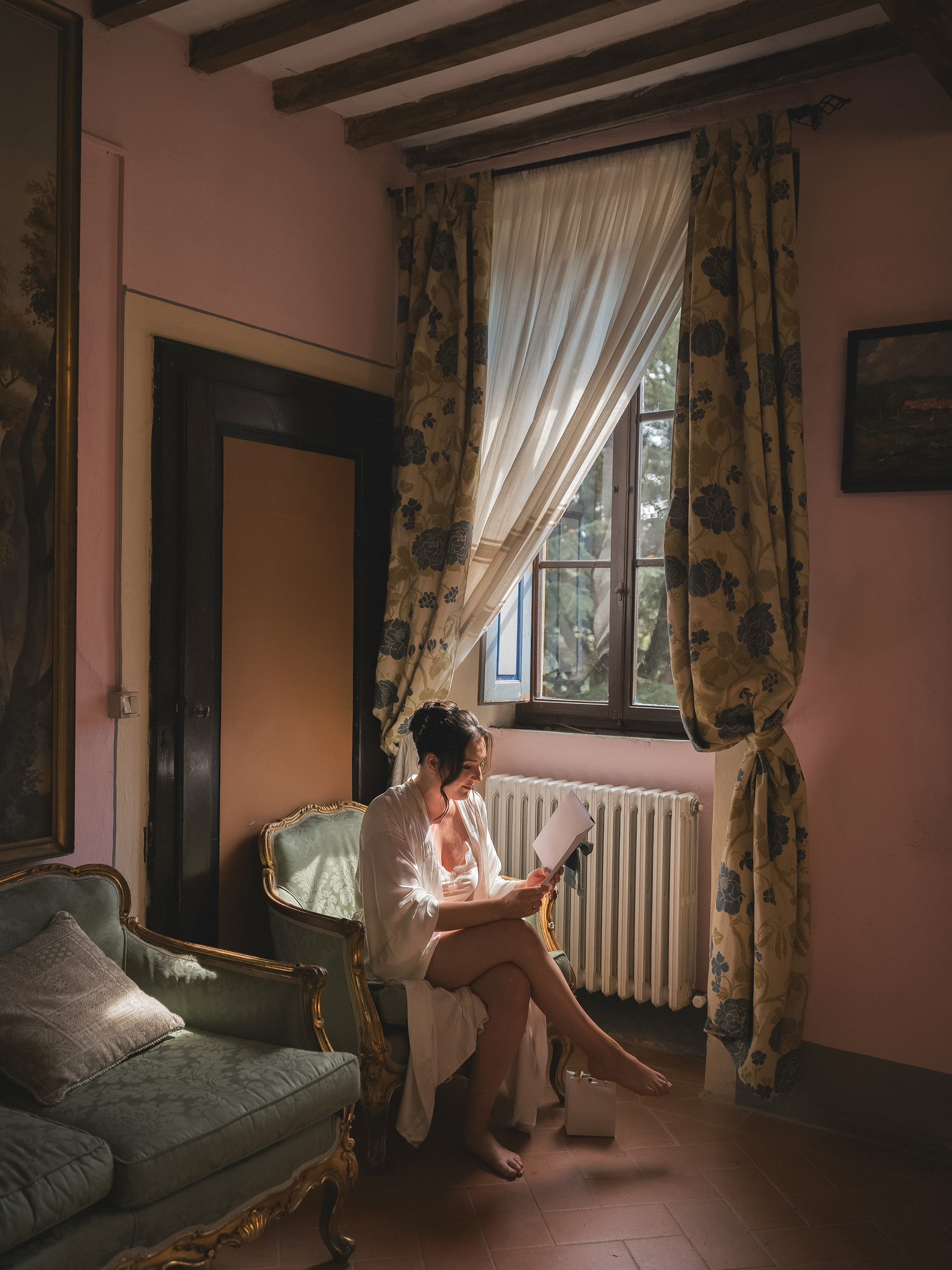 Bride sitting quietly beside a window in warm natural light before her Tuscany wedding ceremony